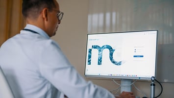 Lääkäri katsoo näyttöä, jolla on Mediconsult Saga -potilastietojärjestelmän kirjautumissivu.