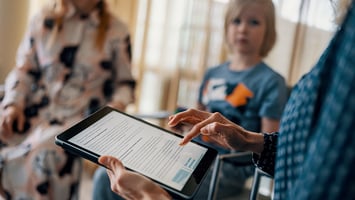 Lapsi katsoo sosiaalityöntekijää, jolla kädessään tabletti.