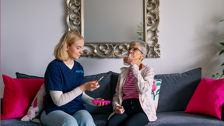 Kotihoidon sairaanhoitaja auttaa vanhusta ottamaan lääkettä